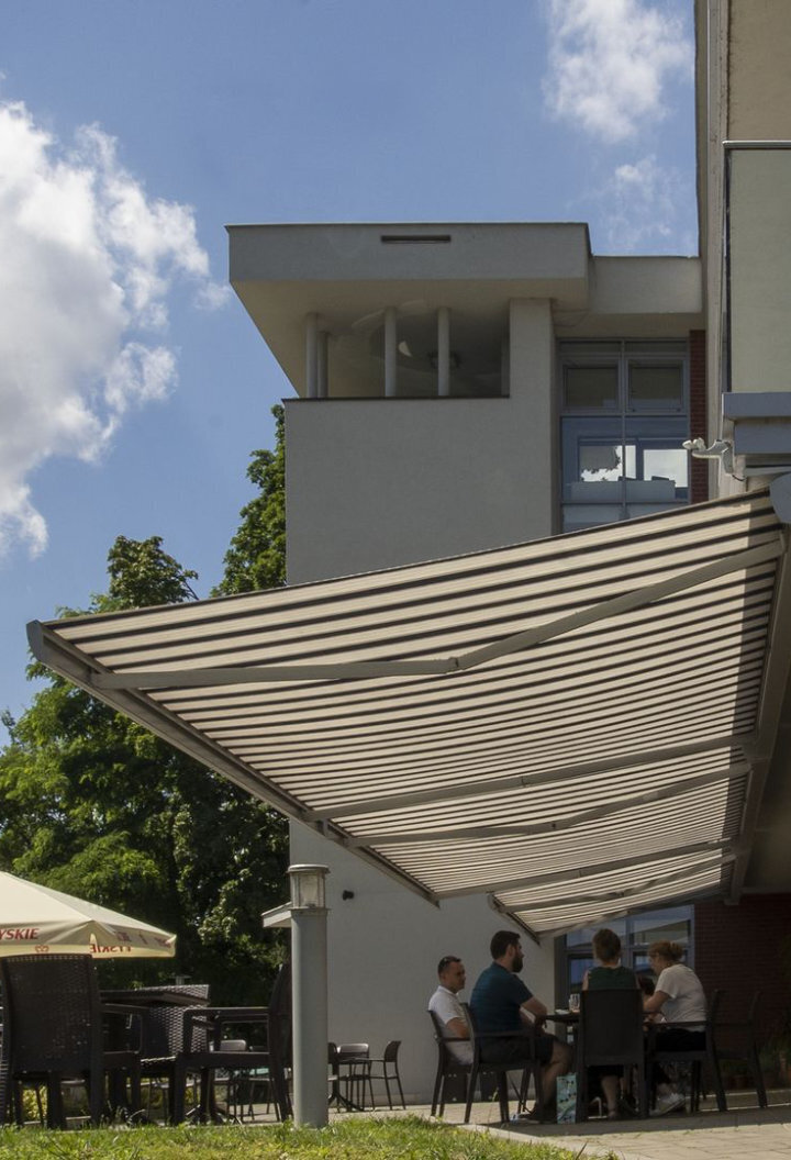 markiza przeciwsłoneczna nad tarasem ludzie siedzą przy stole
